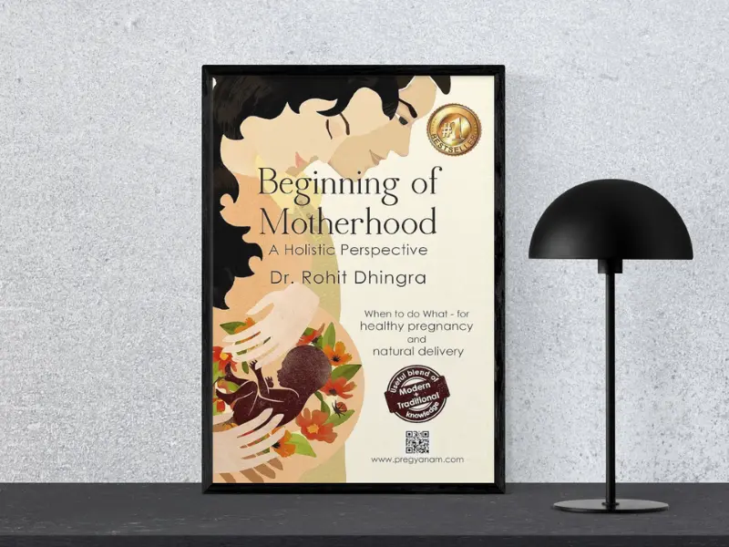 Beginning of Motherhood — A Holistic Perspective Book cover of "Beginning of Motherhood — A Holistic Perspective" by Rohit Dhingra, displayed in a black frame next to a modern black lamp