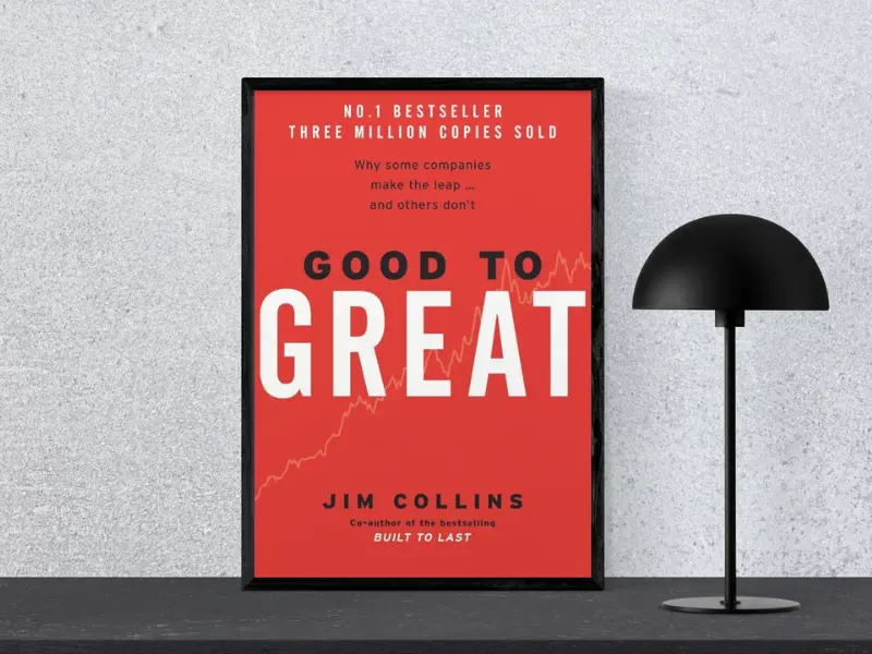 Book cover of "Good to Great by Jim Collins, featuring the subtitle ‘Tiny Changes Remarkable Results’, displayed in a black frame next to a modern black lamp, considered one of the greatest business books.