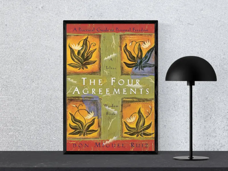 Book cover of "The Four Agreements by Don Miguel Ruiz Toltec, featuring the subtitle ‘Tiny Changes Remarkable Resutls’, displayed in a black frame next to a modern black lamp.
