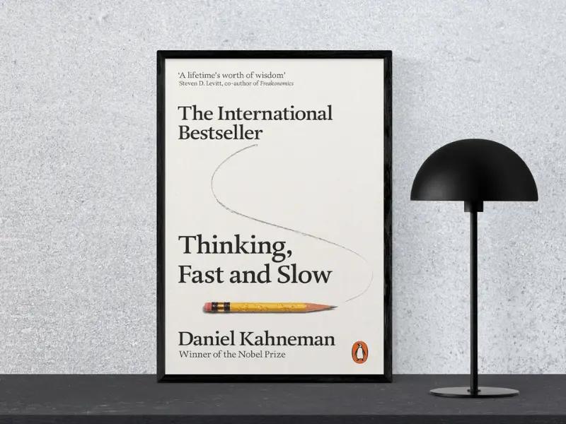Thinking, Fast and Slow by Daniel Kahneman Book cover of Thinking, Fast and Slow by Daniel Kahneman, featuring the subtitle ‘Tiny Changes Remarkable Results’, displayed in a black frame next to a modern black lamp, highlighting