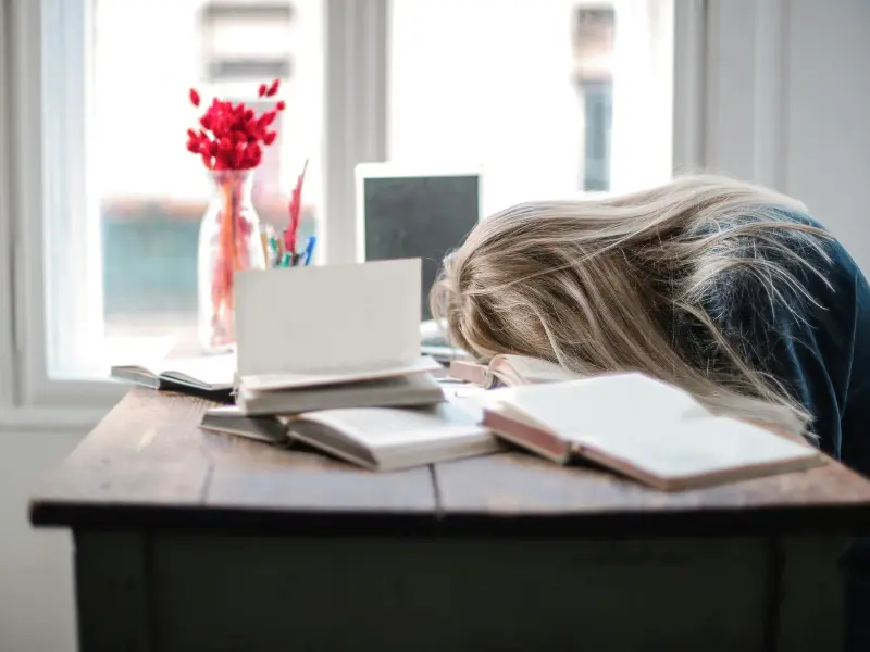 “Student sitting at a study table, smiling and raising one hand with excitement. Symbolizes positive student mental health, confidence, and motivation after overcoming stress and academic pressure.”
