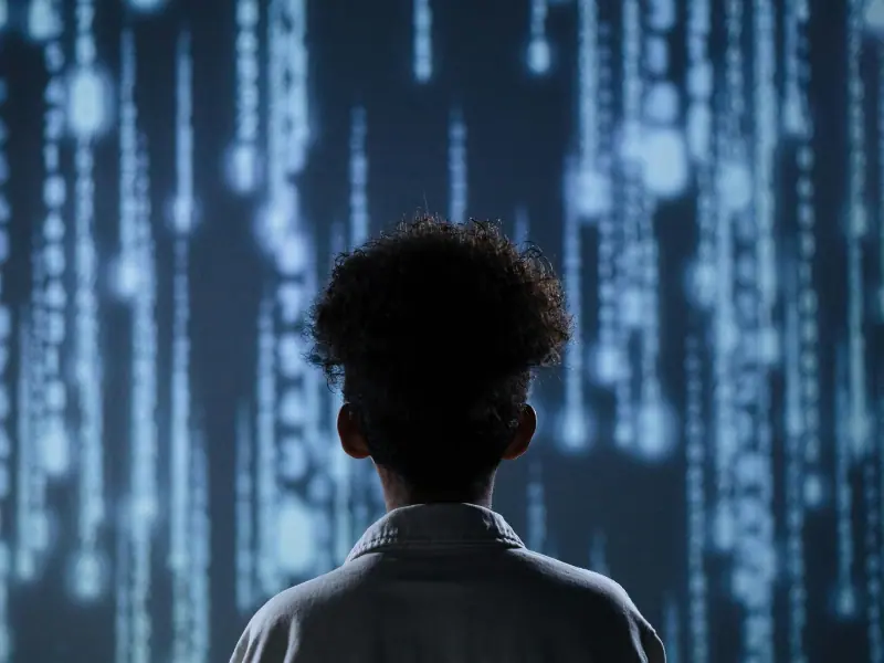 The Power of Observation A person with curly hair stands before a digital screen filled with falling code, symbolizing deep focus and the power of observation in a tech-driven world. The futuristic background evokes themes of awareness, attention, and decoding hidden patterns—core traits of successful minds.