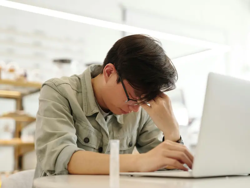 A man wearing off-white shirt and working on laptop but it seems he is not living his a happy life. he is upset