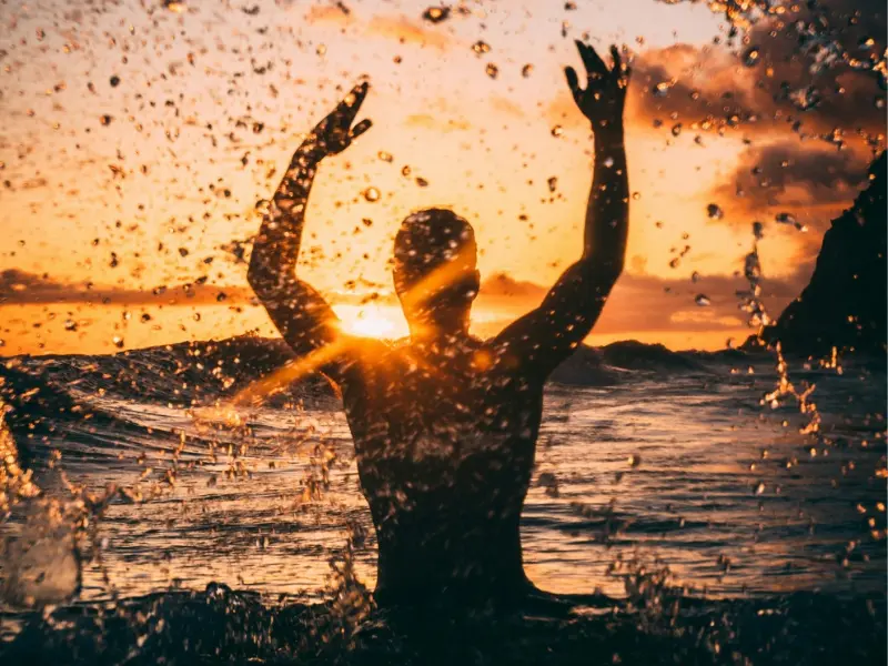 Man raising his arms and having sun bath in the river showing he is living a happy life